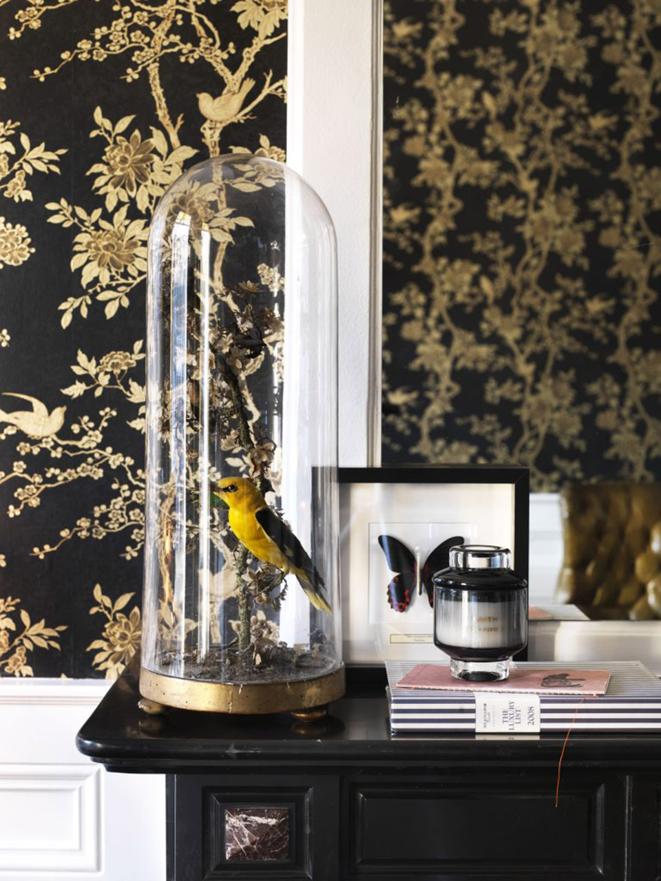 A yellow bird under a glass dome against gilded floral wallpaper